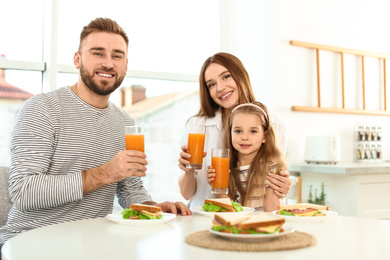 Photo of Happy family having breakfast with sandwiches at table in kitchen