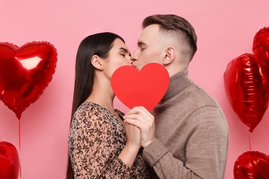 Photo of Lovely couple kissing behind red paper heart on pink background. Valentine's day celebration