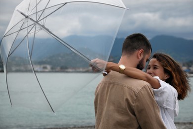 Young couple with umbrella enjoying time together under rain on beach