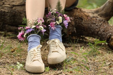 Woman sitting on log with flowers in socks outdoors, closeup