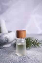Bottle of aromatic essential oil and mortar with pine branch on light grey table, closeup. Space for text
