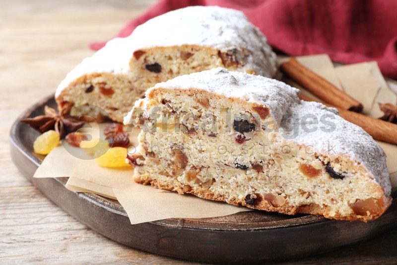 Wooden plate of cut delicious Stollen sprinkled with powdered sugar on table, closeup