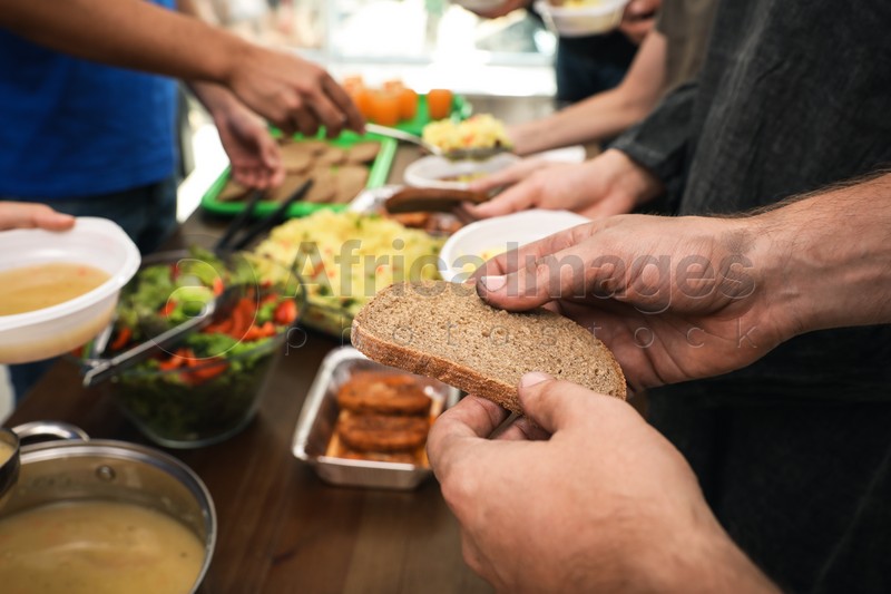 Poor man holding slice of bread at table in charity centre, closeup
