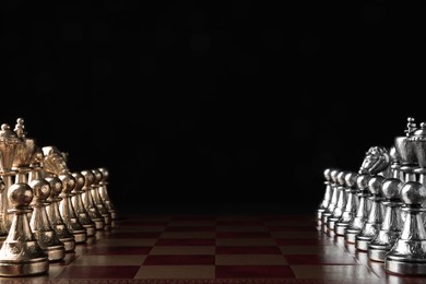 Chessboard with game pieces on black background. Space for text