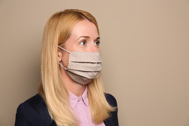 Woman wearing handmade cloth mask on beige background, space for text. Personal protective equipment during COVID-19 pandemic