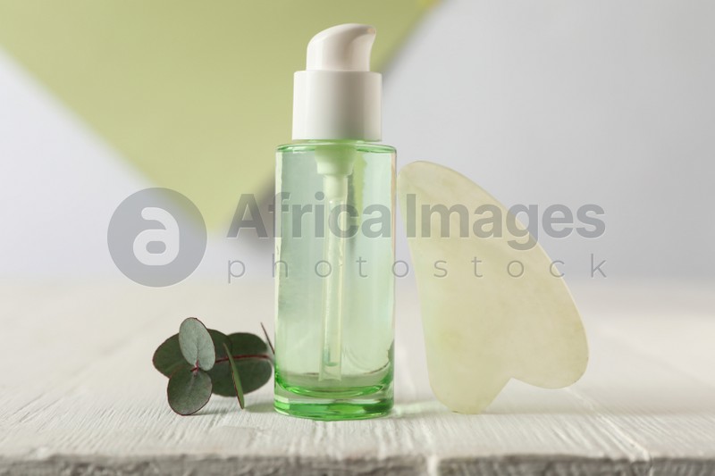 Photo of Jade gua sha tool and skin care product on white wooden table