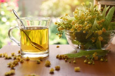 Glass cup of aromatic tea with spoon and linden blossoms on wooden table against blurred background