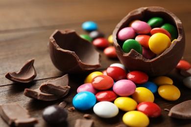 Broken chocolate egg and colorful candies on wooden table, closeup
