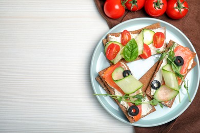 Tasty rye crispbreads with salmon, cream cheese and vegetables served on white wooden table, flat lay. Space for text