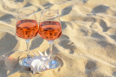 Photo of Glasses of tasty rose wine and seashell on sand, space for text
