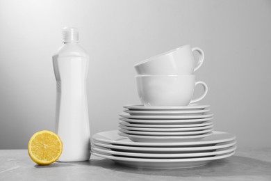 Photo of Set of clean tableware, dish detergent and lemon on grey table against light background