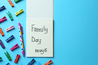 Notebook with text Family Day May 15, pen and decorative clothespins on light blue background, flat lay. Space for design
