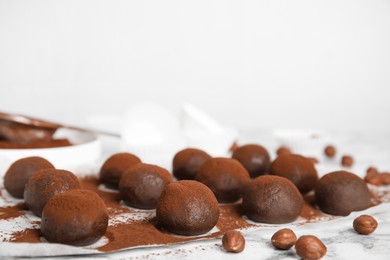 Delicious chocolate truffles with cocoa powder and hazelnuts on white marble table, space for text