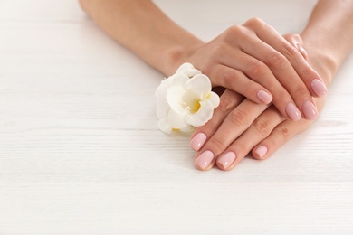 Closeup view of woman with flower at white wooden table, space for text. Spa treatment