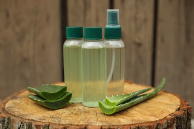 Photo of Bottles of cosmetic products and sliced aloe vera leaves on wooden stump