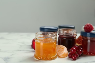 Jars of different jams and ingredients on white marble table, space for text