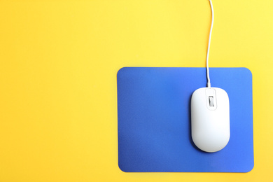 Photo of Modern wired optical mouse and pad on yellow background, top view. Space for text
