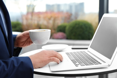 Photo of Businessman with laptop and coffee in outdoor cafe, closeup. Corporate blog