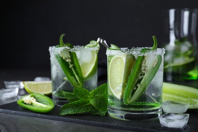Photo of Spicy cocktail with jalapeno, cucumber and lime on black table