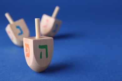 Hanukkah traditional dreidel with letters Pe and He on blue background, space for text