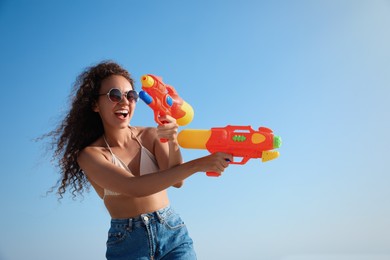 African American woman with water guns having fun against blue sky