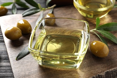 Glass bowls of oil, ripe olives and green leaves on black wooden table, closeup