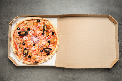 Photo of Delicious seafood pizza in box on grey table, top view
