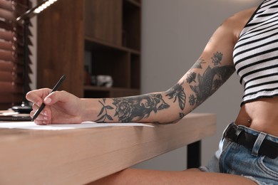 Woman with tattoos on arm drawing in sketchbook at table, closeup