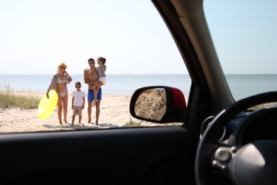 Happy family with inflatable ring at beach, view from inside of car