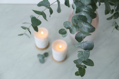 Beautiful eucalyptus branches and burning candles on grey table, closeup. Interior element
