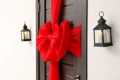 Photo of Wooden door with beautiful red bow and lanterns hanging on wall. Christmas decoration