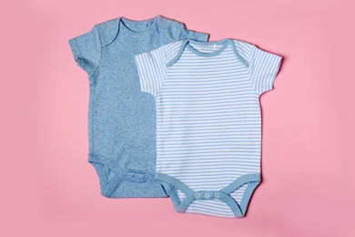 Cute baby onesies on color background, top view