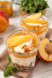 Tasty peach yogurt with granola, pieces of fruit and jam on white wooden table