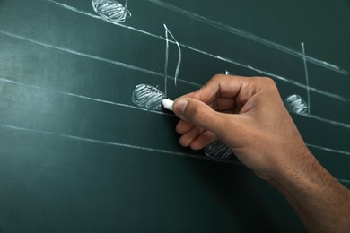 Teacher writing music notes with chalk on greenboard, closeup