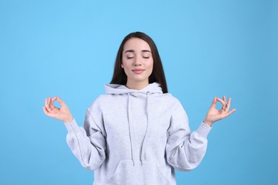 Young woman meditating on light blue background. Stress relief exercise