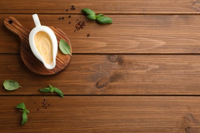 Tasty sauce in gravy boat, basil leaves and spice on wooden table, flat lay. Space for text