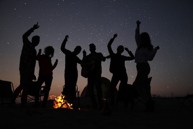 Group of friends having party near bonfire in evening. Camping season