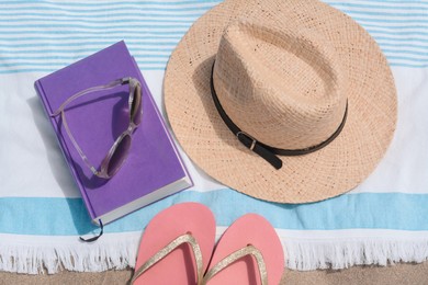 Beach towel with straw hat, book, sunglasses and flip flops on sand, flat lay
