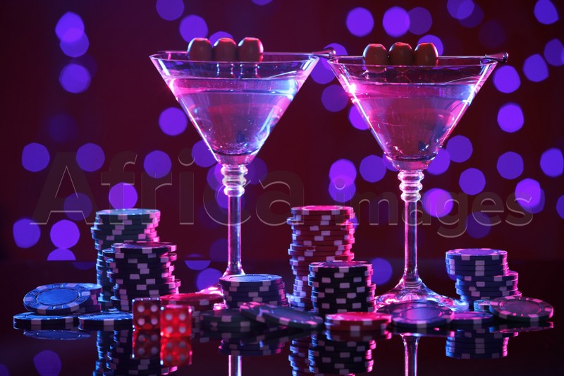 Cocktail, dice and casino chips on table against blurred lights