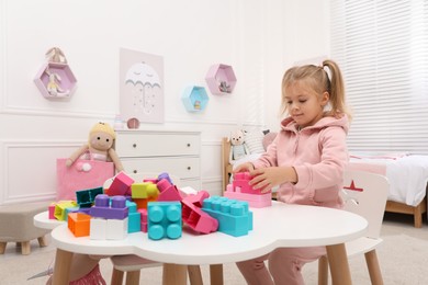 Cute little girl playing with colorful building blocks at table in room, space for text
