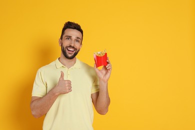 Man with French fries on yellow background, space for text