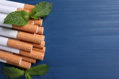 Menthol cigarettes and mint leaves on blue wooden table, flat lay. Space for text