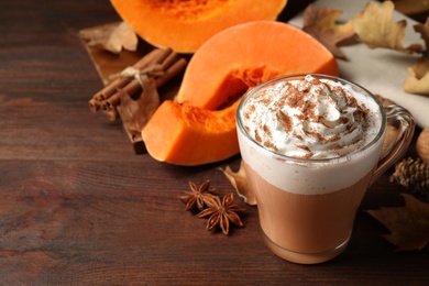 Delicious pumpkin latte and ingredients on brown wooden table, closeup. Space for text