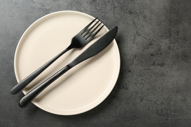 Photo of Beige ceramic plate with cutlery on grey table, top view. Space for text