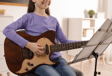 Little girl playing guitar at music lesson, closeup. Learning notes