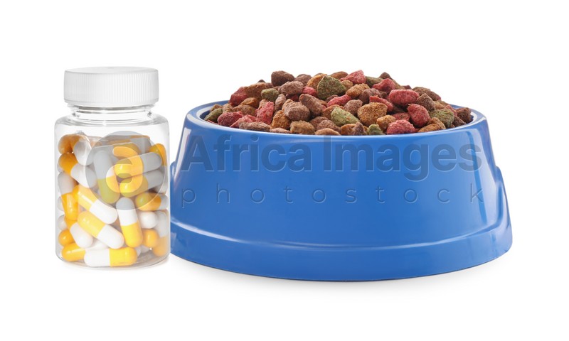 Dry pet food in feeding bowl and bottle with vitamin pills on white background