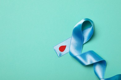Photo of Light blue ribbon with paper blood drop on turquoise background, top view and space for text. Diabetes awareness