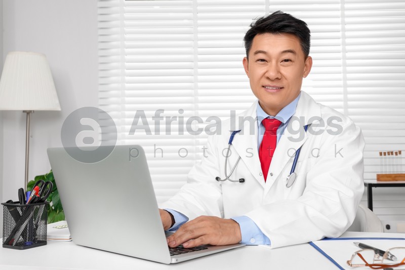 Photo of Happy doctor with laptop consulting patient at white desk in clinic. Online medicine