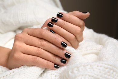Woman with black manicure holding knitted fabric, closeup. Nail polish trends