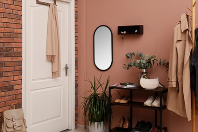 Photo of Hallway interior with green plants and wooden hanger for keys on pale pink wall
